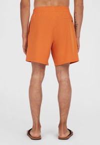 Bañador naranja con cintura elástica, bolsillos laterales y un bolsillo trasero. Fabricado con material ligero, de corto tamaño y textura suave.