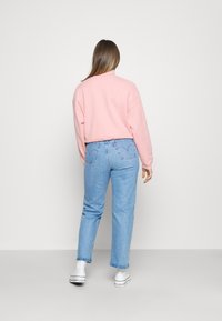 Sweatshirt rosa claro com ombros caídos, combinado com jeans de denim azul claro com bolsos traseiros. Ténis brancos completam o look.