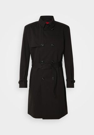 Abrigo negro de trench con diseño de doble botonadura, grandes botones, cintura con cinturón y cuello alto. Tejido suave con un acabado mate.