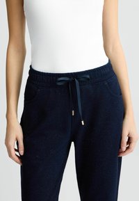Pantalons de jogging bleu marine avec une finition texturée, dotés d'une taille élastique avec cordon, de poches latérales et de points dorés sur le cordon.