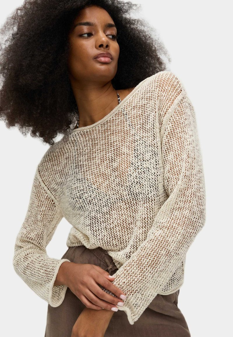Pull léger de couleur crème en maille, présentant une trame ouverte, un col large et des manches longues avec une coupe décontractée. Fini texturé.