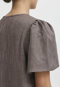 Top din in de culoare maro, cu mâneci scurte tip puff, decolteu rotund și detalii subtile cu dungi verticale pentru un interes vizual texturat.