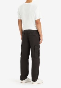 Svarta cargobyxor med flera sidofickor, i bomullsmaterial, något lös passform, kombinerade med en vit t-shirt med kort ärm och vita sneakers.