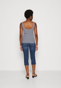Top a righe in blu navy e bianco, abbinato a jeans blu a vita alta. Il top presenta una scollatura profonda sul retro. Indossato con sandali neri e orecchini a cerchio.