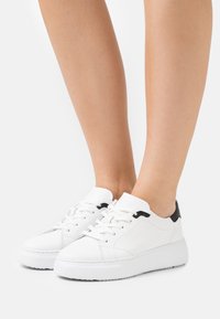 Weiße Leder-Sneaker mit schwarzen Akzenten an der Ferse, runder Zehenpartie, flacher Gummisohle und Schnürdesign. Glatte Textur mit Nähdetails.