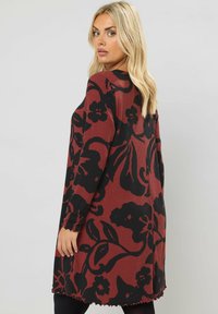 Rippkleid in Maroon mit großem schwarzen Blumenmuster, ausgestattet mit langen Ärmeln und einem gezackten Saum. Die Silhouette ist entspannt und midi-länglich.