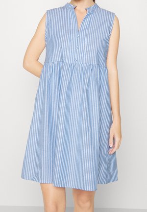 Bezrekawkowa sukienka w pionowe niebiesko-białe paski, z guzikami z przodu i marszczonym pasem, noszona przez stojącą osobę.