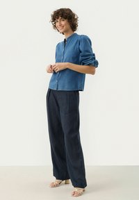 Denimskjorta med knappar, rund halsringning och puffärmar, i kombination med löst sittande mörka byxor och sandaler med remmar i beige.