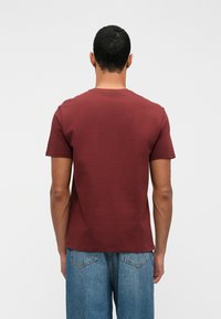 Burgundská tričko s krátkym rukávom a okrúhlym výstrihom, zobrazené zozadu. Hladký bavlnený materiál, priliehavý strih, v kombinácii s svetlomodrými džínsy.