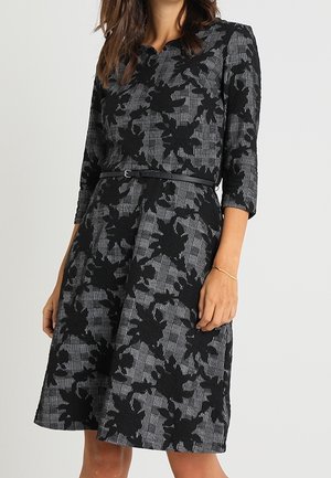 Robe noire avec un textile gris texturé, ornée d'un motif floral en dentelle, manches trois-quarts, taille cintrée et jupe évasée.