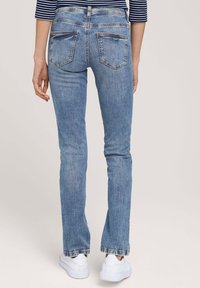 Jeans de mezclilla de color azul claro con corte ajustado, que presentan bolsillos traseros, ligeros desgastes y dobladillos deshilachados. Combinados con zapatillas blancas.