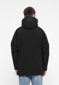 Svart polstret jakke med hette, med en glatt tekstur, lange ermer og en litt forlenget lengde, designet for varme og komfort.