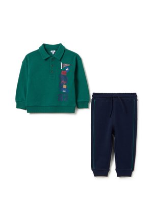 Polo en coton vert à manches courtes, avec des motifs de texte colorés ; associé à un pantalon de survêtement bleu marine avec des rayures vertes sur les côtés.