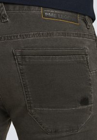 Donkergrijze jeans van gestructureerde stof, met een achterzak, gestikte details en een leren label met merknaam en gele accenten.