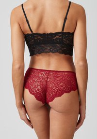 Zwarte kanten bralette en rode kanten hipster slipjes, met bloempatronen, gegolfde randen, zichtbare bandjes, doorschijnende textuur, achteraanzicht.