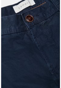 Pantalon en coton bleu marine à la texture lisse, avec une fermeture à bouton marron et des coutures oranges contrastantes. Étiquette de marque visible.