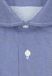 Blauwe overhemd met een klein rond patroon, witte knopen en een puntige kraag.