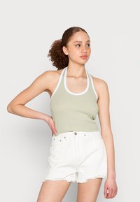 Top halter verde claro com uma textura canelada, apresentando detalhes em branco. Combinado com calções de ganga brancos de cintura alta, desfiados na bainha.