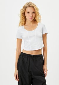 Hvid cropped t-shirt med korte ærmer, rund halsudskæring og vertikale sømdetaljer. Sammen med løstsiddende sorte bukser.