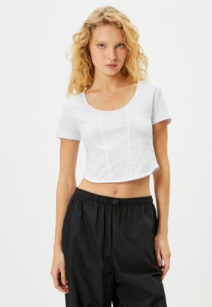 Hvid cropped t-shirt med korte ærmer, rund halsudskæring og vertikale sømdetaljer. Sammen med løstsiddende sorte bukser.