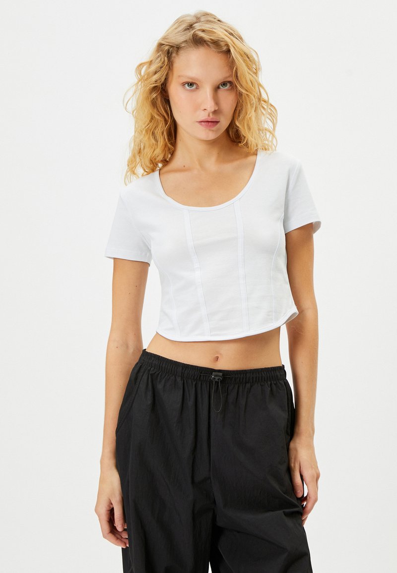 Hvid cropped t-shirt med korte ærmer, rund halsudskæring og vertikale sømdetaljer. Sammen med løstsiddende sorte bukser.