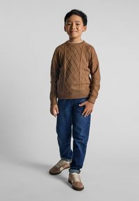 Maglione lavorato a maglia marrone con motivi a diamante, jeans blu e sneakers marrone chiaro. Il maglione ha un collo rotondo e polsini a coste.
