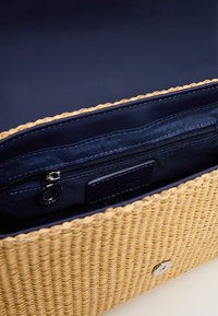 Borsa intrecciata in paglia con esterno marrone chiaro, interno blu scuro, tasca con zip e logo argentato, caratterizzata da un design strutturato e testurizzato.