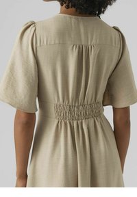 Vestido beige con mangas cortas y abullonadas, que presenta un detalle de cintura fruncida y una tela suave y texturizada. La parte trasera tiene un escote sencillo y limpio.