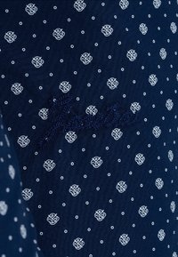 Laivastonsininen kangas valkoisilla kuvioiduilla pisaroilla, jossa on tekstuurinen brodeeraus yksityiskohtana kauniilla kursiivilla. Silkkinen pinta, lähikuva.