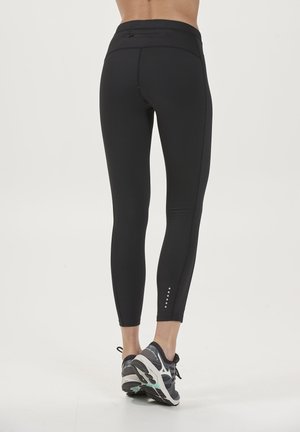 Leggings noirs avec taille haute, tissu extensible et texture lisse. Comprend une poche au dos et des accents à pois aux chevilles.
