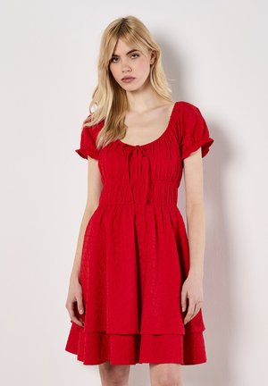 Robe courte rouge avec un décolleté carré, des manches courtes bouffantes et une taille élastique. Elle présente une jupe à volants en tissu texturé.
