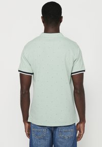 Polo verde con piccoli motivi triangolari, maniche corte e rifiniture a contrasto in blu navy e bianco sul colletto e sulle maniche. Vestibilità classica.