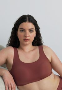 Brun sømløs bralette med rund hals og brede stropper, laget av glatt, elastisk materiale, med et minimalistisk design.