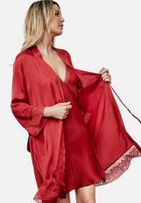 Robe en satin rouge avec des bordures en dentelle, dotée de larges manches et d'un décolleté en V profond. Léger et fluide, il tombe élégamment autour du corps.