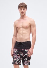 Mustad ujumispüksid roosade ja roheliste lillemustritega. Materjal näib õhuke; vöökohal on nöör, ülaosas on kontrastne osa.