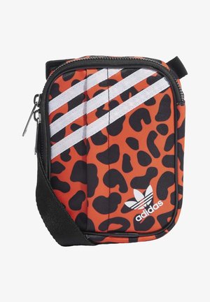 Pomarańczowa i czarna torebka na ramię w panterkę z białym logo Adidas i trzema białymi ukośnymi paskami, czarnym zamkiem błyskawicznym oraz regulowanym czarnym paskiem.