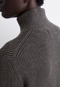 Pull à col roulé gris côtelé avec un col haut, présentant des lignes verticales texturées et une finition lisse sur le col et les épaules.
