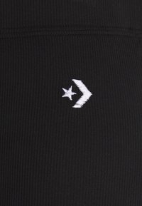 Vitt broderat stjärna och chevron-logotyp på svart ribbat tygbakgrund.