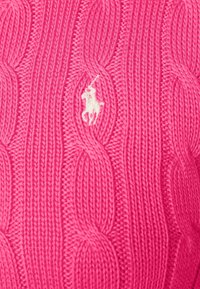 Tissu en maille torsadée rose avec une figure brodée blanche représentant une personne à cheval tenant un maillet de polo.