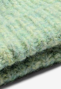 Viegli zaļa teksturēta sega, kas izgatavota no mīksta, pūkaina materiāla ar ribotu dizainu. Slāņi parāda krāsu un dziļuma atšķirības.