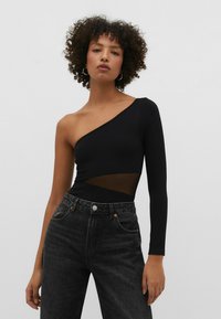 Bodysuit noir avec une manche longue et un panneau en mesh transparent à la taille, associé à un jean gris foncé taille haute.