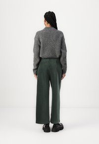 Maglione grigio lavorato a maglia con una vestibilità ampia, abbinato a pantaloni verdi a gamba larga realizzati in tessuto testurizzato e scarpe con plateau nere.