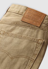 Beige denim jeans met een bruine leren patch met "Levi Strauss & Co." en het logo, met contrasterende stiksels en een gebogen zaknaad.