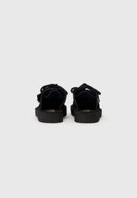 Sandales en suède noir avec une texture douce, présentant un dos arrondi, une semelle épaisse et des accents de lacets noués pour un ajustement réglable.