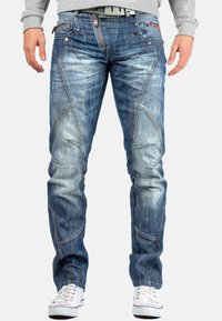 Jean en denim bleu avec une coupe slim, finition délav�ée et détails de couture asymétriques. Comprend plusieurs poches et une fermeture éclair.