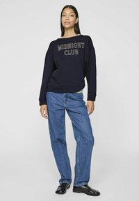 Sudadera navy con "MIDNIGHT CLUB" en costura contrastante, combinada con jeans de pierna ancha azules. Tejido suave, corte holgado, puños acanalados.
