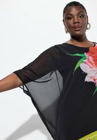 Camisón negro transparente con un gran estampado floral en tonos de rosa y hojas verdes, con mangas de corte holgado y un escote redondeado.