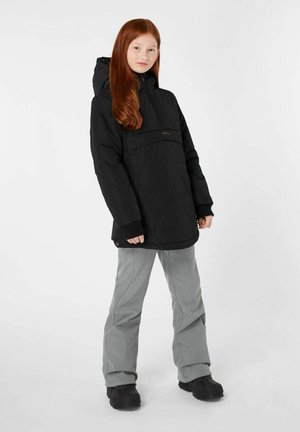 Chaqueta acolchada negra con capucha, que presenta un bolsillo delantero y puños elásticos. Combinada con pantalones gris claro y botas negras.