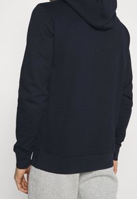 Sudadera azul marino de tela suave, con una gran capucha, mangas largas, puños acanalados y un diseño limpio sin logotipos visibles.