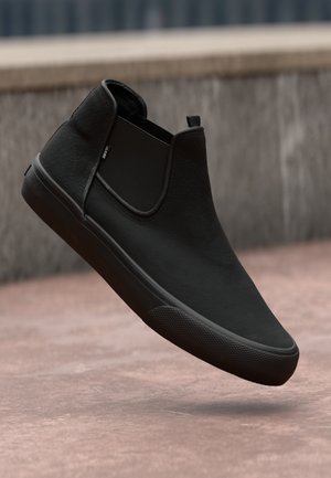 Black slip-on shoe made of textured material with a smooth finish, round toe, and rubber sole featuring a subtle grip pattern.